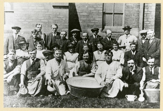 A photograph of Boldon Colliery Soup Kitchen Volunteers 1926, a group photo of men and women, some wearing hats, with a large bucket in the centre of the photo