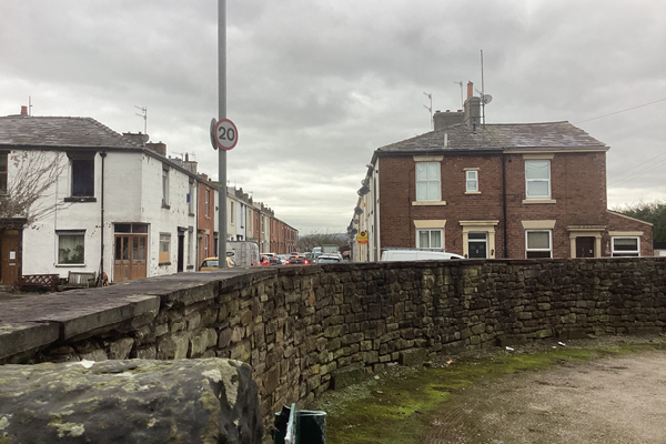 A photograph of a street, Factory Row, in the present day - showing a wall int he foreground, and a row of houses