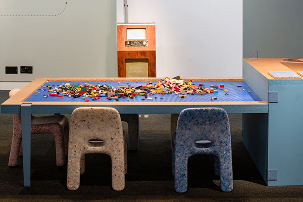 Photograph of Charlie Chairs at table in exhibition.