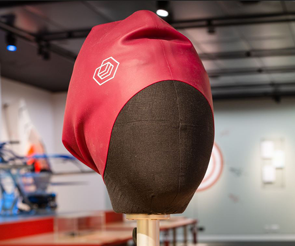 Photograph of Soul Cap: a red swimming cap with room for hair on dummy head in exhibition. 