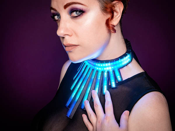 A side profile image of a person looking at the camera, wearing a glowing blue necklace