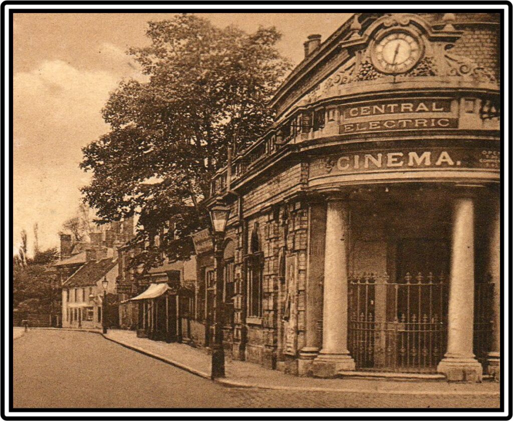 Photograph of a building with pillars with a clokface at the top and the words 'Central Electric Cinema' in capital letters. Next to the building is a road with trees and other buildings