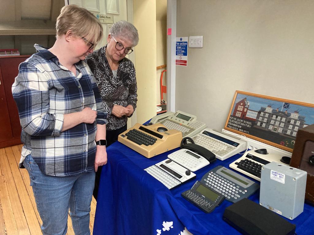 Two people standing over a table that has various pieces of desktop typing equipment on it