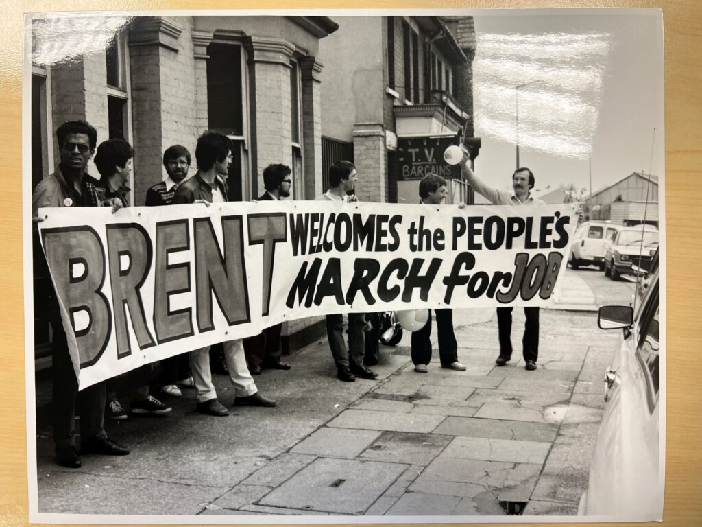 Black and white photo showing eight men standing on the pavement, holding a landscape banner that reads 'Brent welcomes the People's March for Jobs'