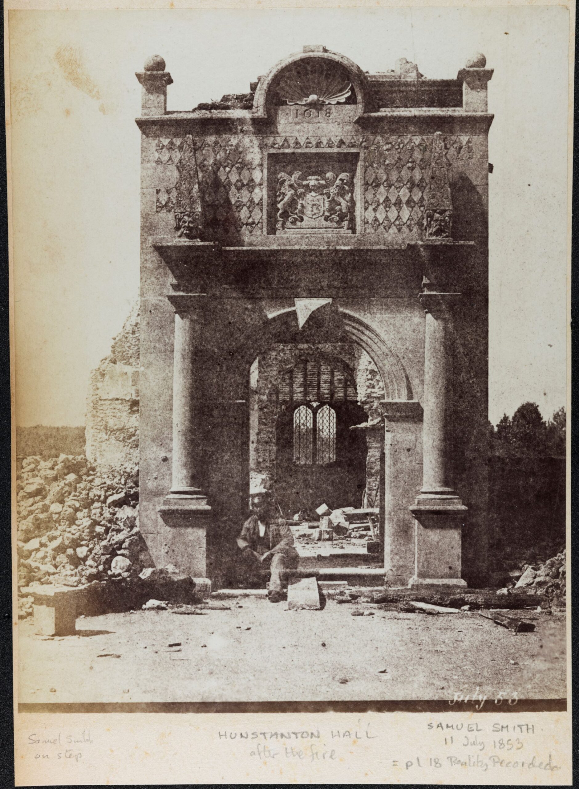 Black and white photo of a severely damaged building. The photo is dated July 1853. A man is sitting on the steps of what remains of a stone building - the photo captions says 'Hunstanton Hall after the fire'.