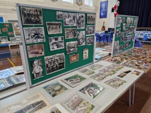 A collection of tables and exhibition boards set up in a school hall. All surfaces are covered with photographs of school children and school grounds.