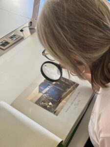 An over-the-shoulder shot of a woman using a magnifying glass to study photos of Hull munitions factory women workers