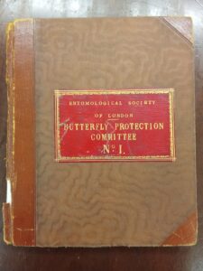 A close up shot of an brown book, with torn edges, and a red label containing the text: 'Butterfly Protection Committee'