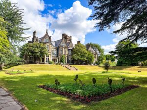 A wide exterior shot showing the Insole Court mansion house in the background, and gardens in the forefront. A flower bed sits directly in the forefront.