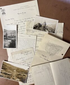 A collection of black and white photographs, hand written letters and journals laid out on a surface.