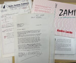 A pile of documents on a desk including a typewritten letter, a document entitled ‘Sheba Feminist Publishers’ and copy of ‘Zami: a new spelling of my name’ by Audre Lorde