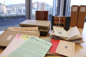 A collection of books, service programmes, documents and carboard boxes resting on a desk.