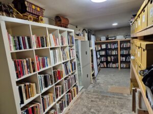 A storage room containing book shelves, cardboard boxes and miscellaneous trinkets including a model horse and carriage.