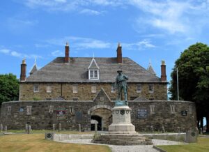 The entrance to a Keep guarded by a concrete curtain wall. In front of the entrance stands the statue of a soldier.