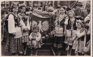 A black and white photograph depicts dozens of women and girls dressed in traditional Polish outfits.