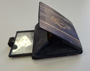 A dark blue powder compact mirror laid open on a plain grey surface.