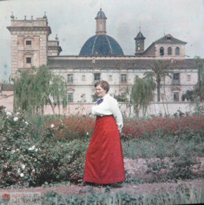 A woman in a white shirt and long red skirt stands in the garden of a museum.
