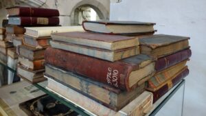 Multiple piles of old books stacked on a glass shelf.