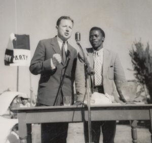 A black and white photograph of two men speaking into a microphone at an outdoor rally.