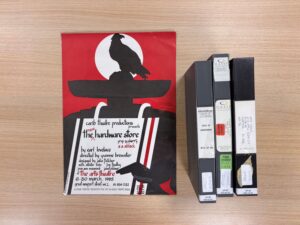 Three video cassettes and an illustration of a crow perched on the hat of a dark figure stood against a red background. These items are laid out on a table.
