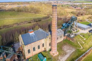 An aerial exterior shot of Pleasley Pit including an old coal mining industrial chimney and metalwork mining tower.